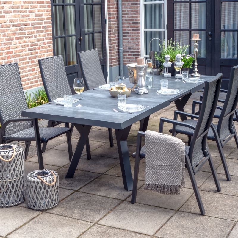 Grande table de jardin rectangulaire avec plateau gris et six chaises noires sur terrasse pavée