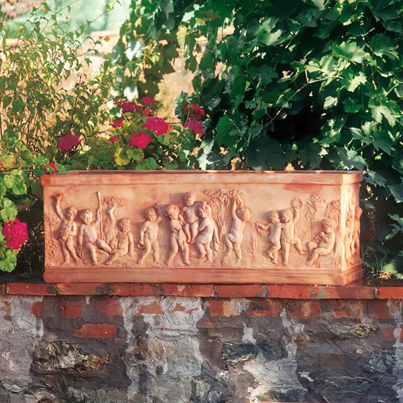Figure de jardin en terre cuite avec un relief de putti, posée sur un mur de pierre avec des plantes de jardin en arrière-plan