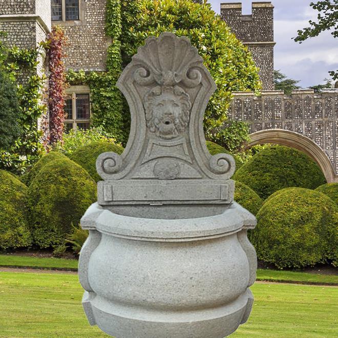 Fontana classica in pietra con testa di leone scolpita in un giardino curato davanti a un edificio storico