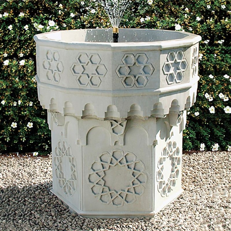 Fontaine claire en pierre avec décorations géométriques florales dans un jardin avec des fleurs blanches