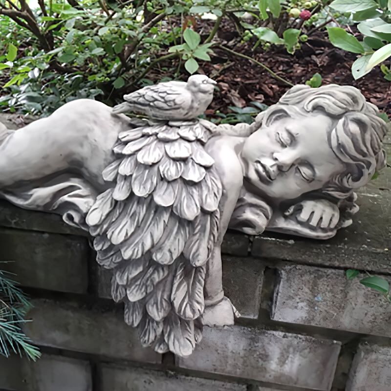 Ange en pierre aux ailes déployées dormant sur un mur dans le jardin