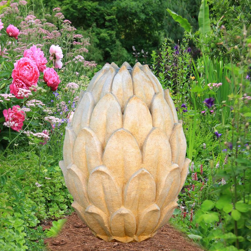 Scultura da giardino color giallo chiaro a forma di carciofo tra piante verdi e rose rosa