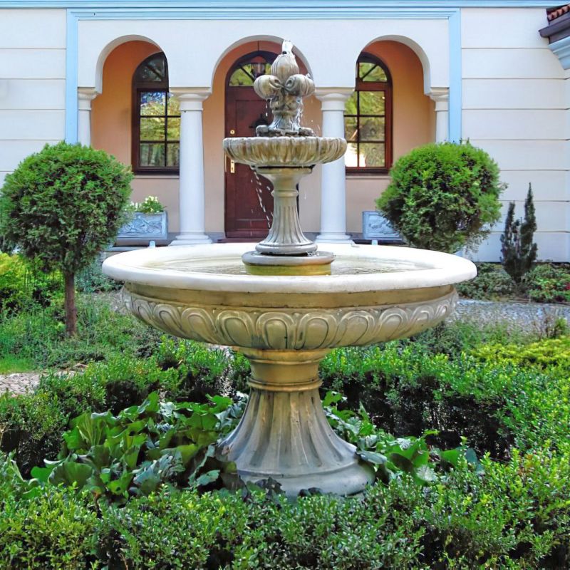 Grande fontana in pietra in giardino circondata da piante verdi davanti a una casa