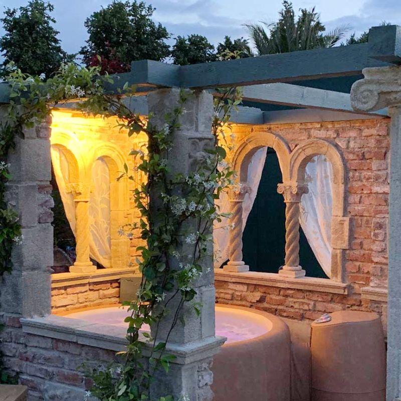 Atmosfera serale in un padiglione da giardino con archi in pietra illuminati e tende bianche