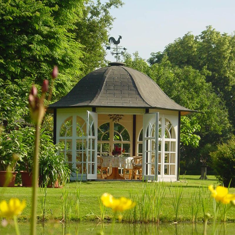 Chalet de jardin blanc avec entrée ouverte, entouré d'herbe verte et d'arbres, décoratif pour le jardin