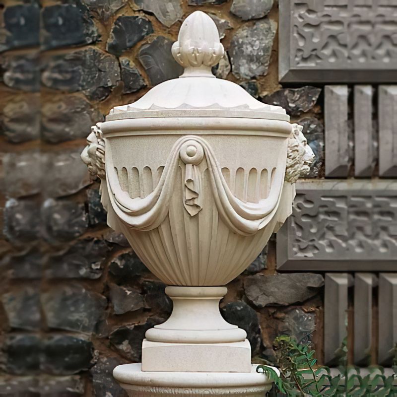 Vase de jardin en pierre blanche ornée devant un mur en pierre