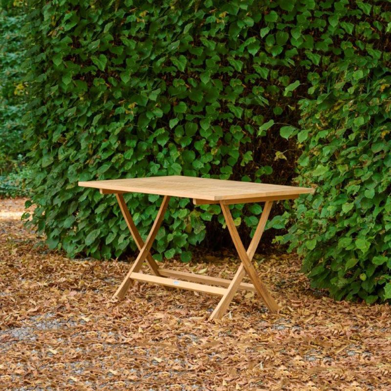 Petite table pliante en bois dans un jardin devant une haie verte
