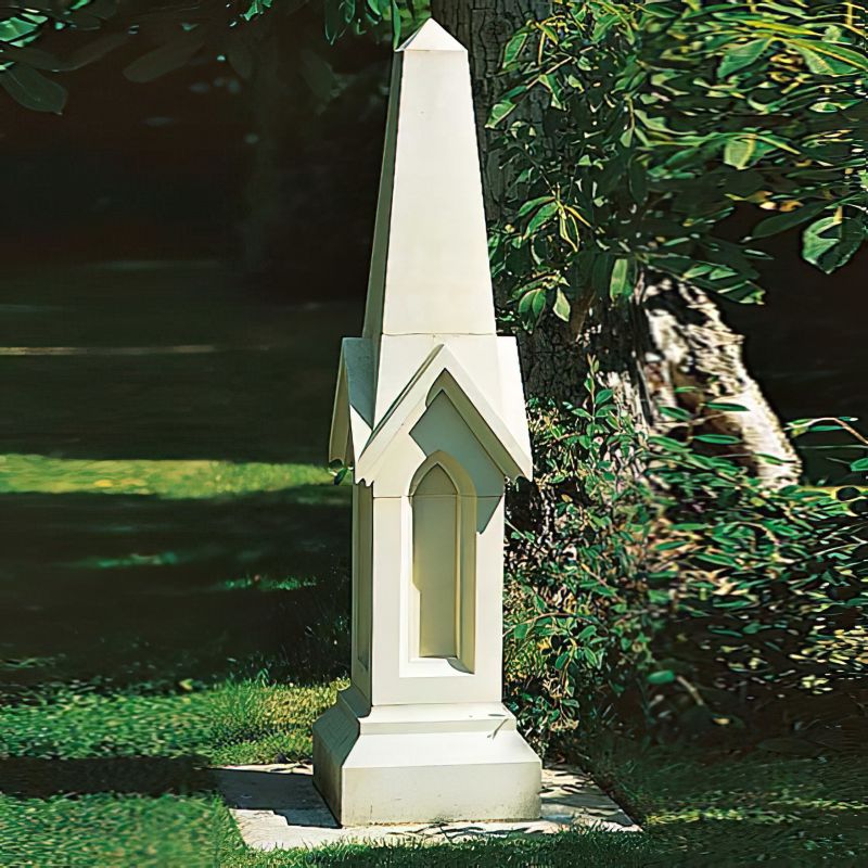 Obélisque de jardin en pierre blanche entourée d'herbe verte et de plantes