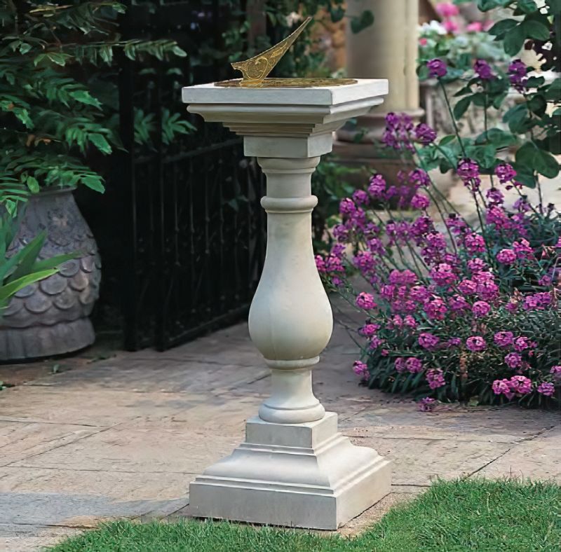 Décoration de jardin avec cadran solaire classique en pierre sur pied de colonne devant des plantes en fleurs