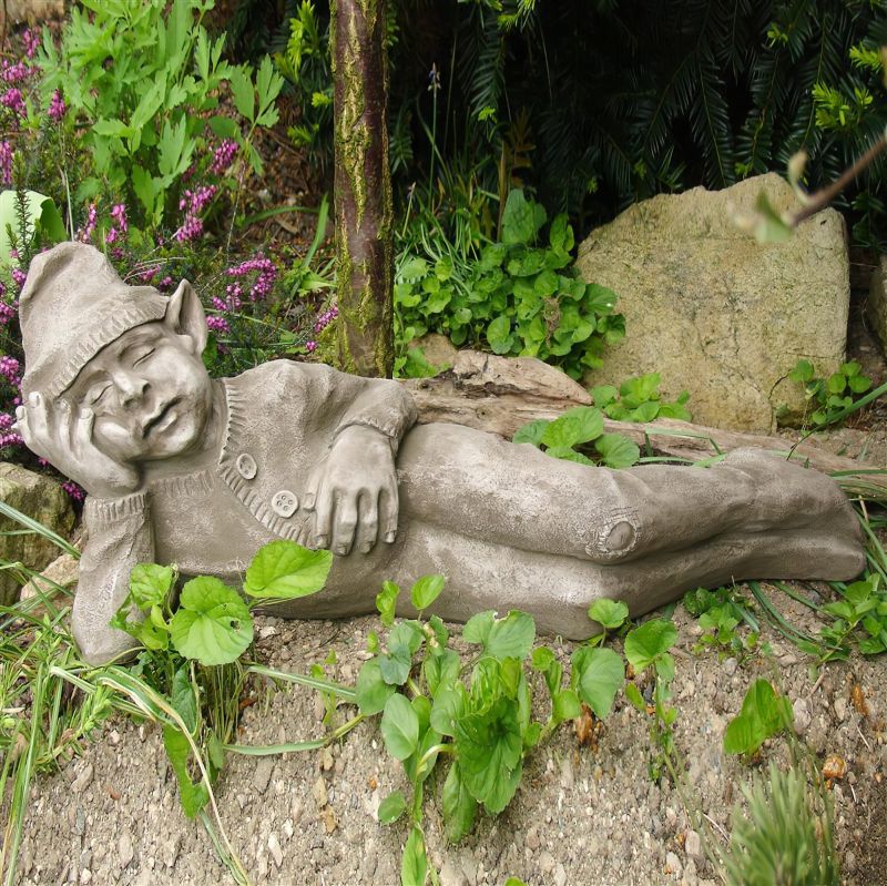 Nain de jardin en pierre allongé entouré de plantes