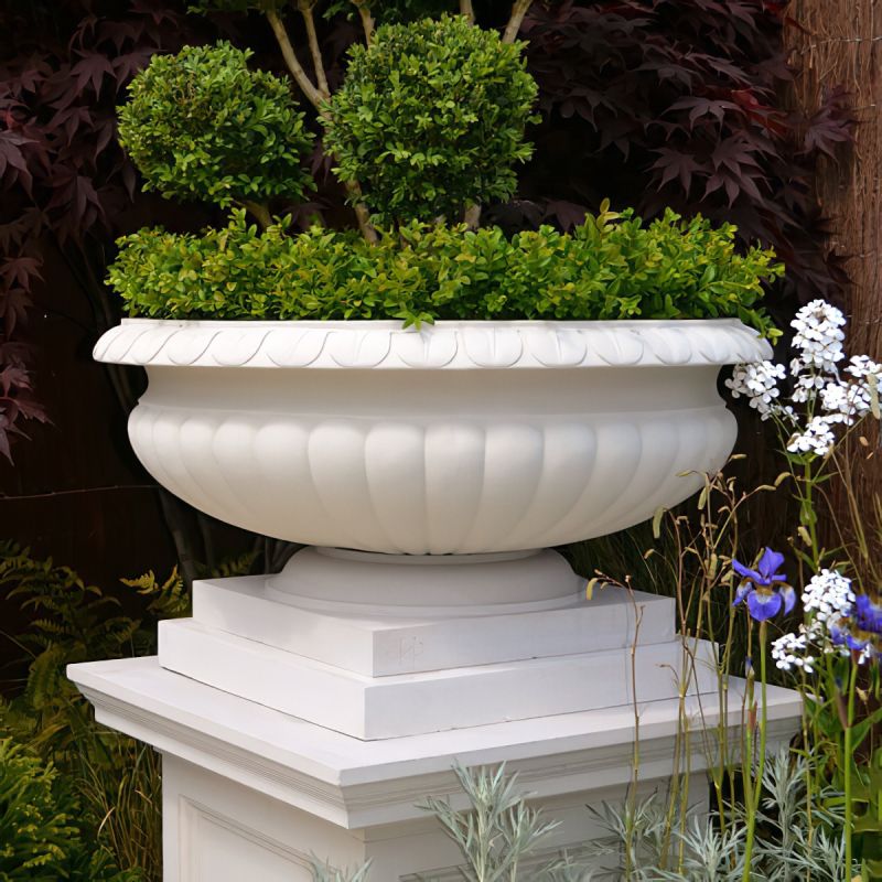 Grand pot blanc avec plantes vertes placé sur un socle dans le jardin